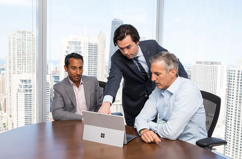 Three business people talking while one is pointing at a laptop on a table